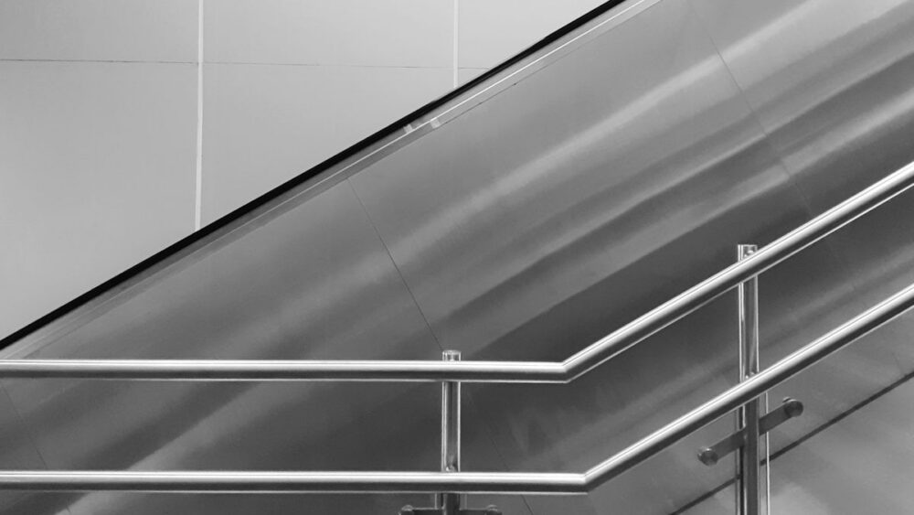 an escalator with stairs and a railing in the foreground, showing multiple uses of stainless steel in architecture